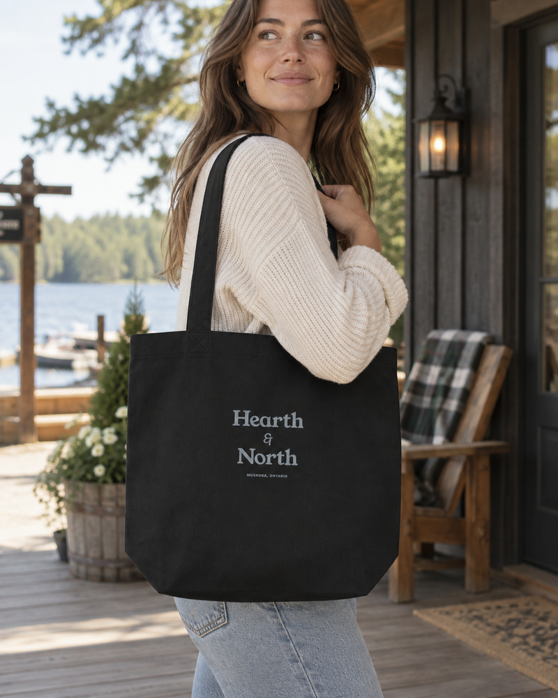 The Tote in black on a shoulder at the dock, stacked Hearth & North wordmark in grey